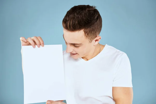Man met een vel papier in zijn handen wit t-shirt bijgesneden uitzicht blauwe achtergrond — Stockfoto