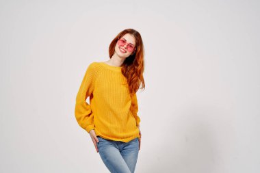 Pembe gözlüklü neşeli kadın elleri sarı süveter stüdyosuyla el kol hareketi yapıyor.