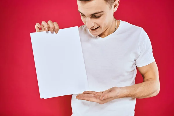 Emotionele man met een vel papier kopieerruimte t-shirt rode achtergrond — Stockfoto