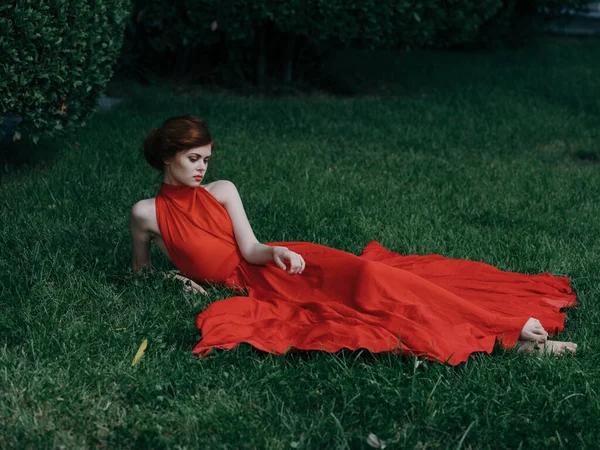 Жінка в червоній сукні лежить на траві гламурна приваблива модель вигляду — стокове фото