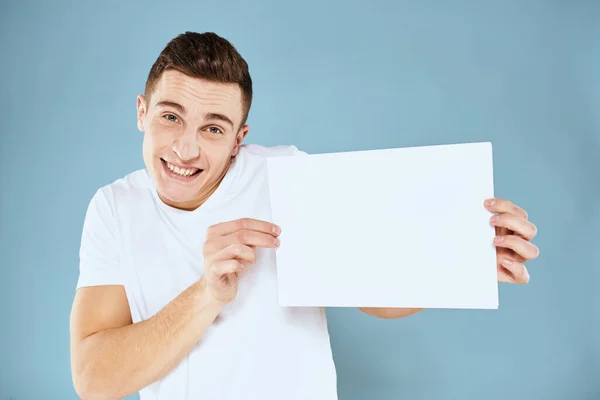 Man met een vel papier in zijn handen wit t-shirt bijgesneden uitzicht blauwe achtergrond — Stockfoto