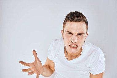 Elleriyle hareket eden duygusal bir adam. Yüz ifadesi hoşnutsuz. Beyaz tişört kesilmiş.