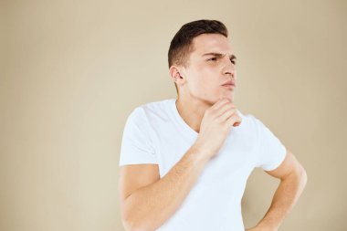 Duygusal erkek yüz ifadesi jesti elleri beyaz tişört bej arka planı