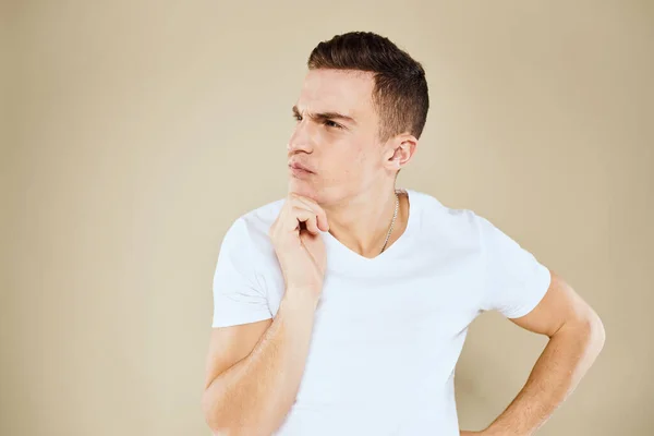 Emotionele man gezichtsuitdrukking gebaar met handen wit t-shirt beige achtergrond — Stockfoto
