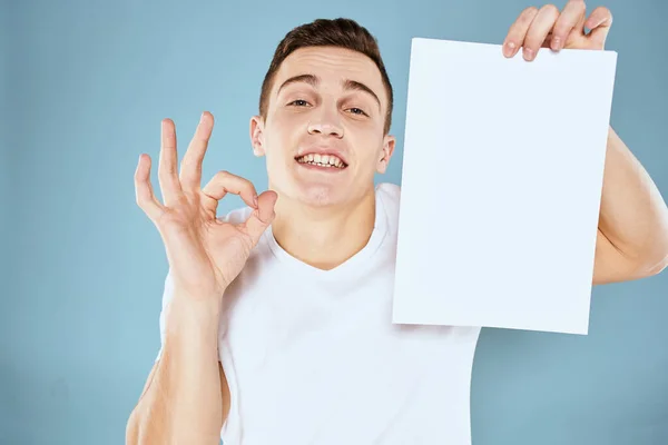 Een man in een wit t-shirt heeft een vel papier kopieerruimte — Stockfoto