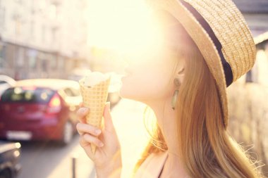 Şapkalı ve dondurmalı güzel bir kadın dışarıda yürüyüş yapıyor.