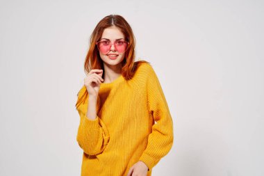 Pembe gözlüklü neşeli kadın elleri sarı süveter stüdyosuyla el kol hareketi yapıyor.