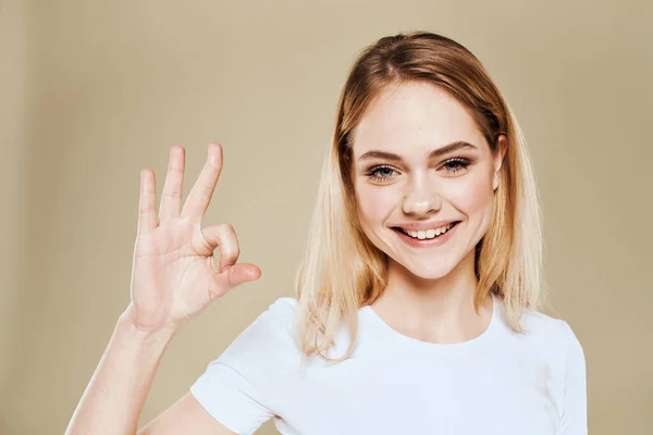Mulher loira alegre em um branco gestos camiseta com suas emoções da mão fundo bege — Fotografia de Stock