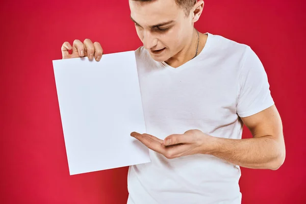 Emotionele man met een vel papier kopieerruimte t-shirt rode achtergrond — Stockfoto