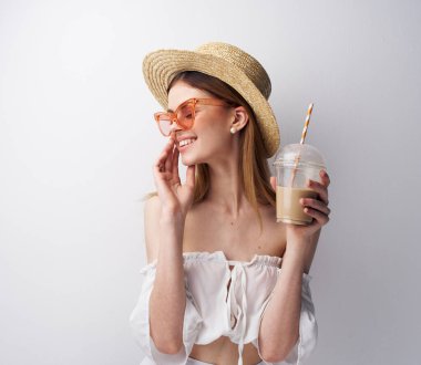 Moda kıyafetleri giyen, şapka takan ve kokteyl içen güzel bir kadın.