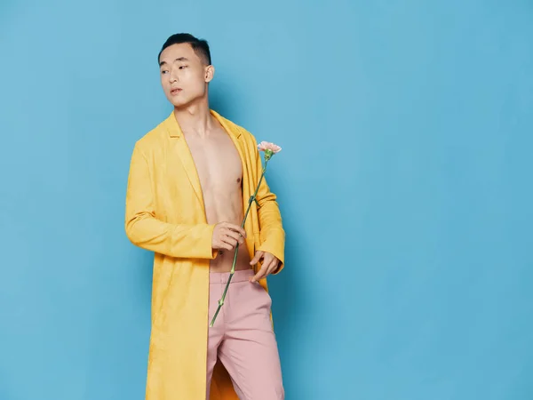 Um homem de casaco amarelo num tronco nu e uma flor nas mãos de calças cor-de-rosa — Fotografia de Stock