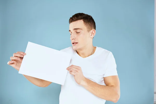 Een man in een wit t-shirt heeft een vel papier kopieerruimte — Stockfoto