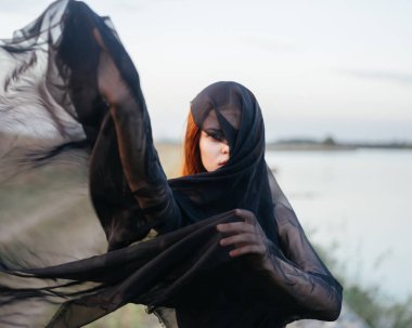 Yüzünde siyah bir eşarp olan bir kadın doğada nehrin kenarında