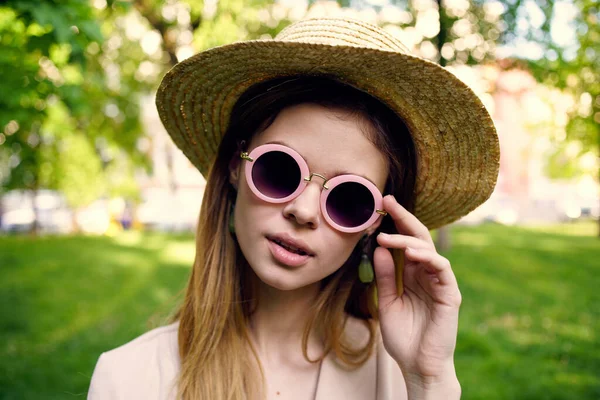 Glada kvinna i hatt bär solglasögon utomhus i parken gräs promenad — Stockfoto