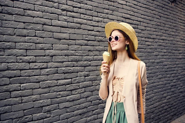 Kvinna i solglasögon och en hatt med glass går genom stadens tegelvägg utomhus — Stockfoto