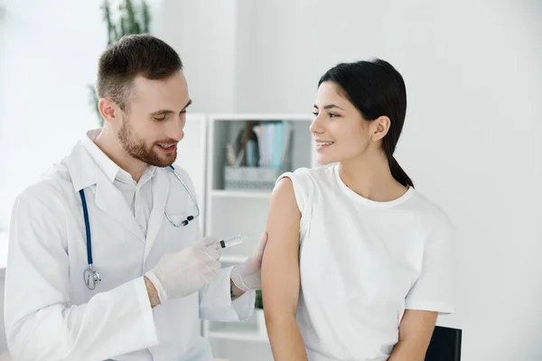 医師は軽い背景で白いTシャツを着た女性の肩にワクチンを注射し — ストック写真