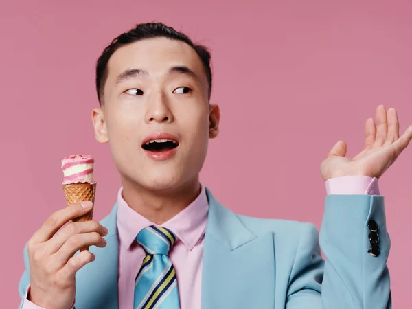 Boldog ázsiai férfi eszik fagylalt rózsaszín háttér kék klasszikus öltöny közelkép — Stock Fotó