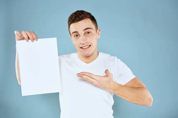 Een man in een wit t-shirt houdt in zijn handen een vel papier emoties bijgesneden weergave van een blauwe achtergrond Copy Space — Stockfoto