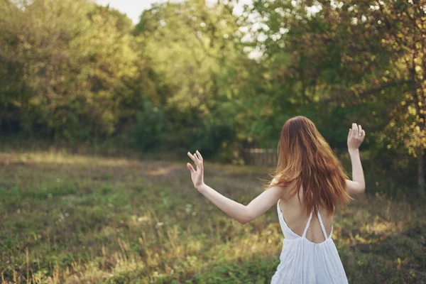 Gelukkig vrouwen in een sundress loopt op groen gras in de weide en bomen op de achtergrond — Stockfoto
