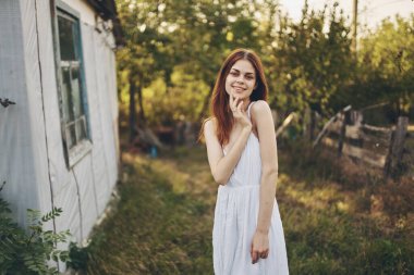 Binanın yakınında beyaz bir elbise içinde mutlu bir kadın ve arka planda ağaçlar.