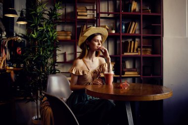 Bir kadın kahve bardağında oturup içki içerken düşünceli bir bakışla rahatlıyor.