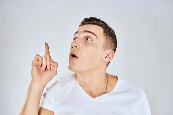 Emotional man in a white t-shirt holds his hand on his face light background — Stock Photo, Image