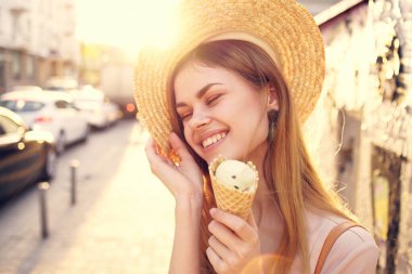 Ellerinde dondurma olan şapkalı bir kadın şehirde yürüyor.