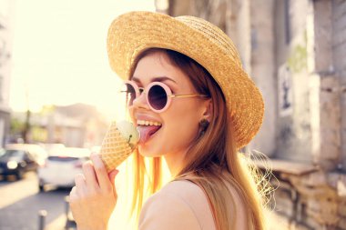 Açık havada şapkalı neşeli güzel kadın ve şehirde yürüyen dondurma.
