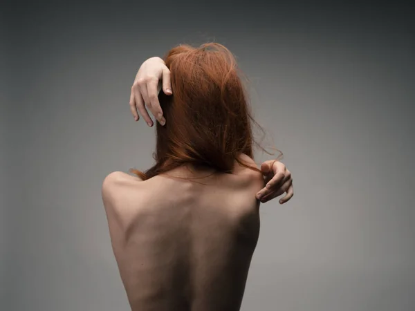 Μια λεπτή κοκκινομάλλα γυναίκα αγγίζει τον εαυτό της με τα χέρια της πίσω από την πλάτη της — Φωτογραφία Αρχείου