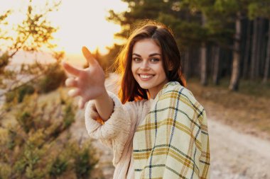 Mutlu kadın doğada gülümsüyor ve arka planda gün batımına doğru elini uzatıyor.