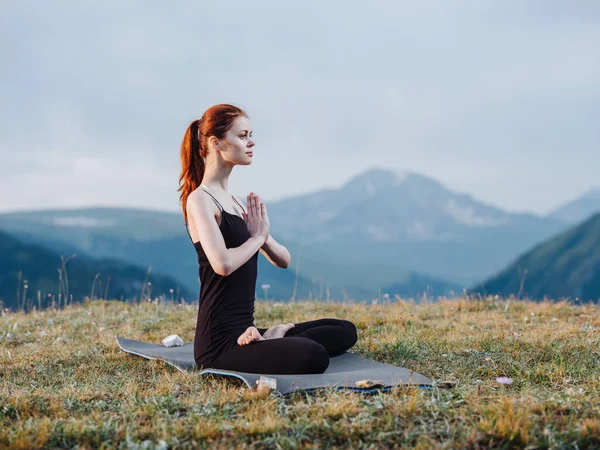 Egy karcsú nő jógázik a hegyekben leggingben és pólóban. — Stock Fotó