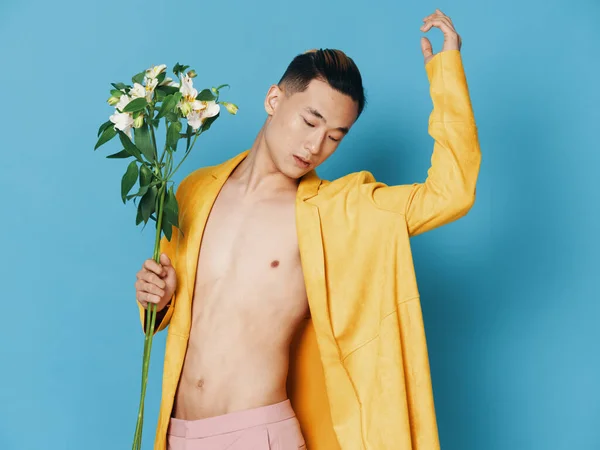 Coreano homem com um buquê de flores em um casaco amarelo gesticulando com as mãos — Fotografia de Stock