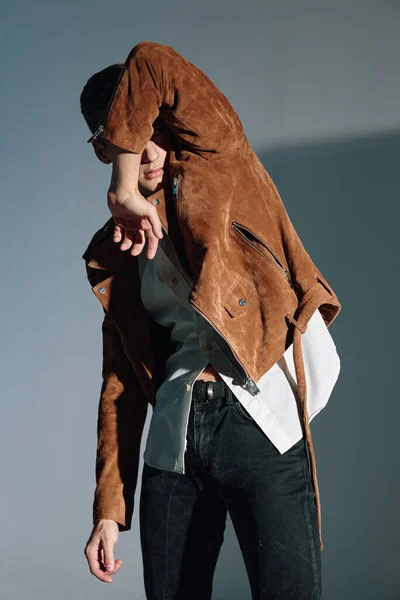 Брюнетка в коричневой куртке закрылась рукой от света на сером фоне. — стоковое фото