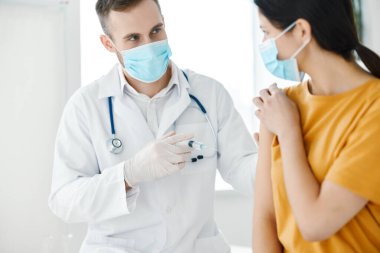 Tıbbi önlüklü bir laboratuvar asistanı elinde şırıngalar ve bir hasta kovid aşısı tutuyor.