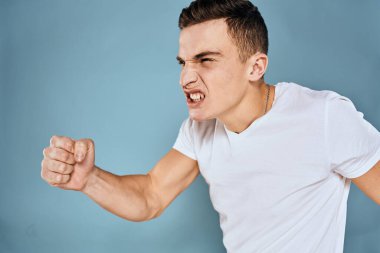 Erkek, duyguları ile hareket eder. Beyaz tişört yüz ifadesi mavi arka plan.