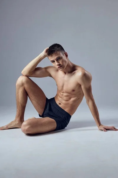 Male athlete sitting on floor with pumped up body posing isolated background — Stock Photo, Image