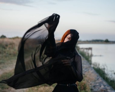 Yüzünde siyah bir eşarp olan bir kadın doğada nehrin kenarında