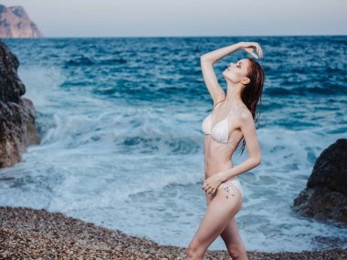 Beyaz mayo giymiş ince bir kadın ellerini okyanus kıyısında gezdirir.