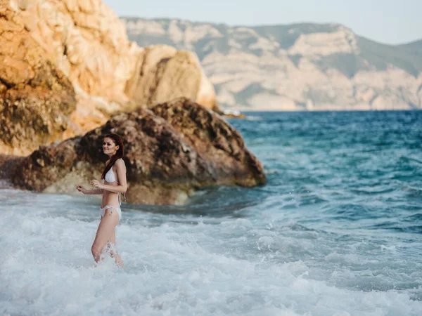 Donna romantica in costume da bagno al mare spiaggia di schiuma bianca e rocce sullo sfondo — Foto Stock