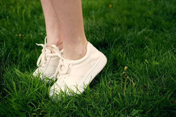 Жінка в білих кросівках в парку йде зеленою травою — стокове фото