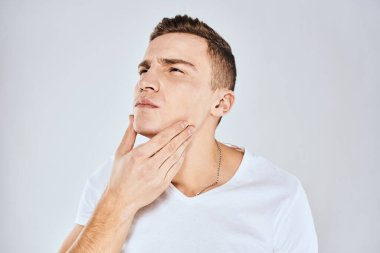 Beyaz tişörtlü duygusal bir adam elini arka planda tutuyor.