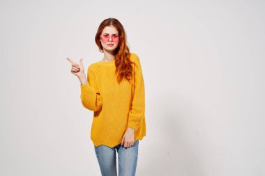 Sarı kazaklı neşeli bir kadın pembe gözlüklü. Duyguları el hareketleriyle ifade ediyor.