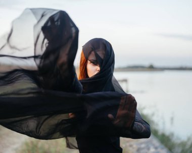 Yüzünde siyah bir eşarp olan bir kadın doğada nehrin kenarında