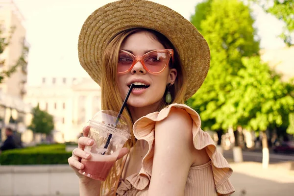 Elegant woman in glasses and a glass hat with a drink outdoors in summer