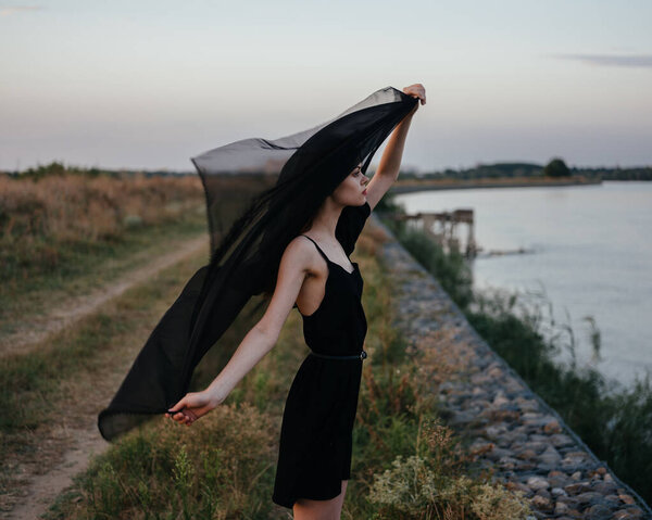 A woman in a black dress with a cloth near her face is resting in nature by the river. High quality photo