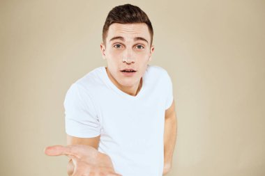 Duygusal erkek yüz ifadesi jesti elleri beyaz tişört bej arka planı