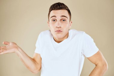 Duygusal erkek yüz ifadesi jesti elleri beyaz tişört bej arka planı