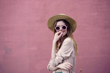 Güneş gözlüklü güzel bir kadın Pembe duvarda yürür