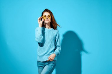 Mavi süveter giyen çekici kadın mavi arka plan pozu veriyor.