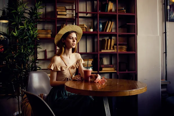 Μια γυναίκα κάθεται σε ένα καφέ σε ένα ποτήρι τραπέζι με ένα ποτό χαλαρωτικό σκεπτικό βλέμμα — Φωτογραφία Αρχείου